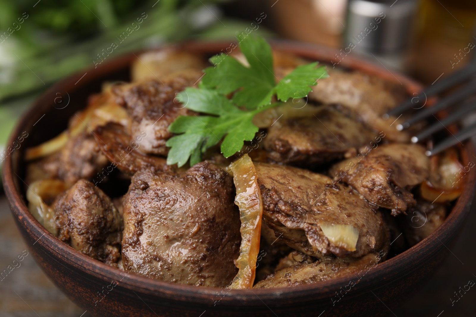 Photo of Tasty fried chicken liver with onion and parsley in bowl on table, closeup