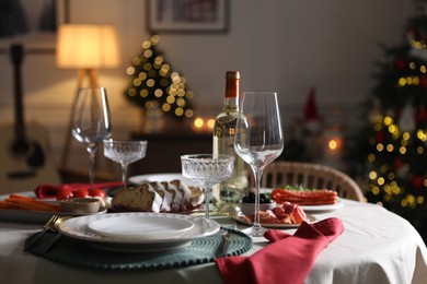 Photo of Christmas table setting with bottle of wine, appetizers and dishware indoors