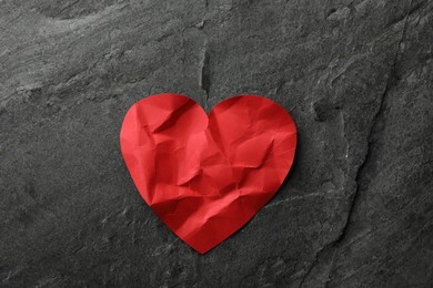 Photo of Crumpled red paper heart on dark grey table, top view. Broken heart