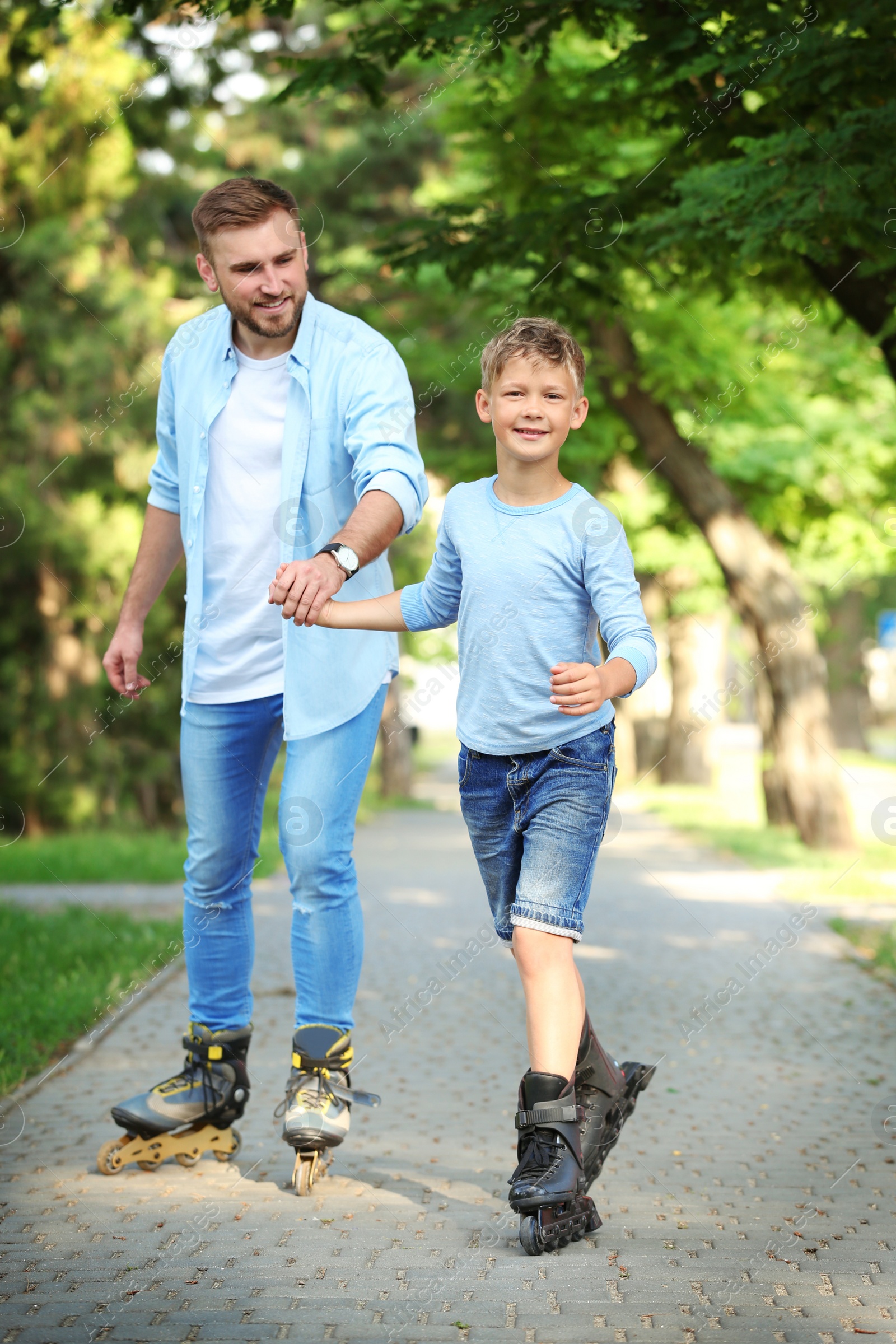 Photo of Father and son roller skating in summer park