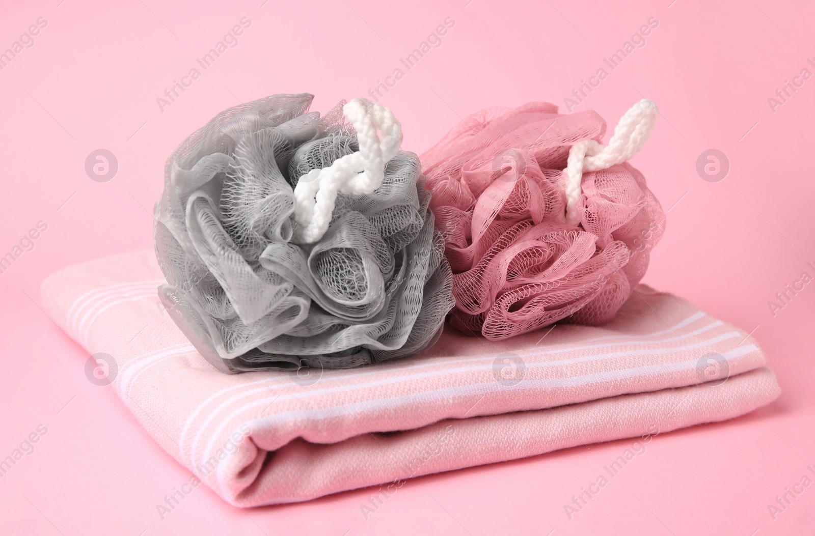 Photo of Colorful shower puffs and towel on pink background