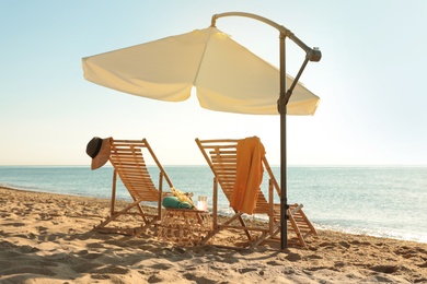 Wooden deck chairs, outdoor umbrella and beach accessories near sea. Summer vacation
