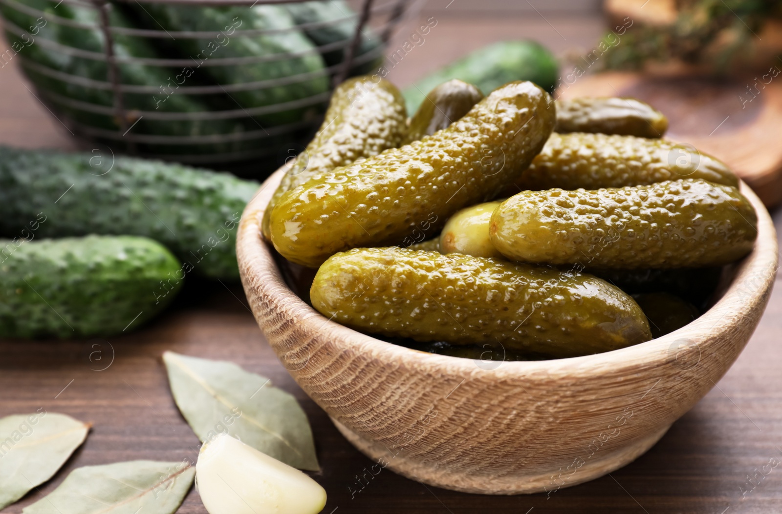 Photo of Bowl of pickled cucumbers and ingredients for food preservation on wooden table, closeup