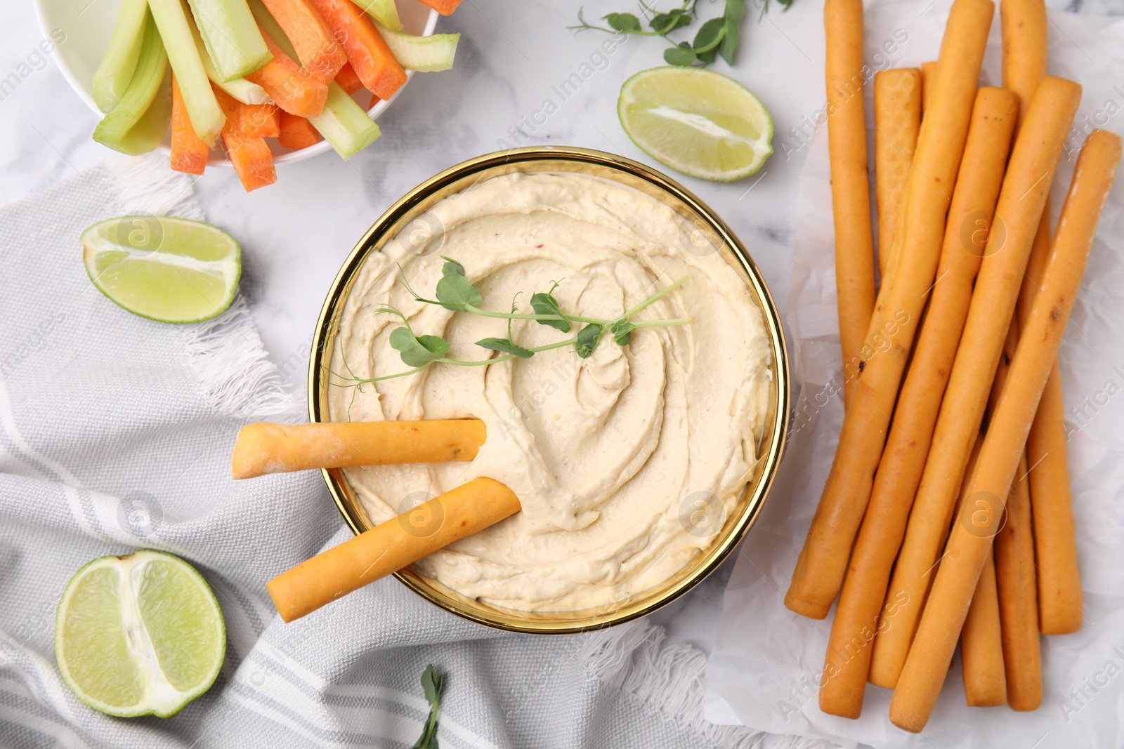 Photo of Delicious hummus with grissini sticks served on white marble table, flat lay