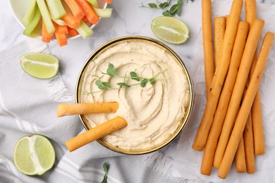 Delicious hummus with grissini sticks served on white marble table, flat lay