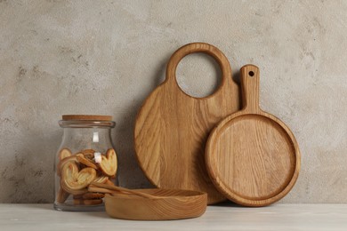 Wooden cutting boards, french palmier cookies, plate and spoons on white table near textured wall