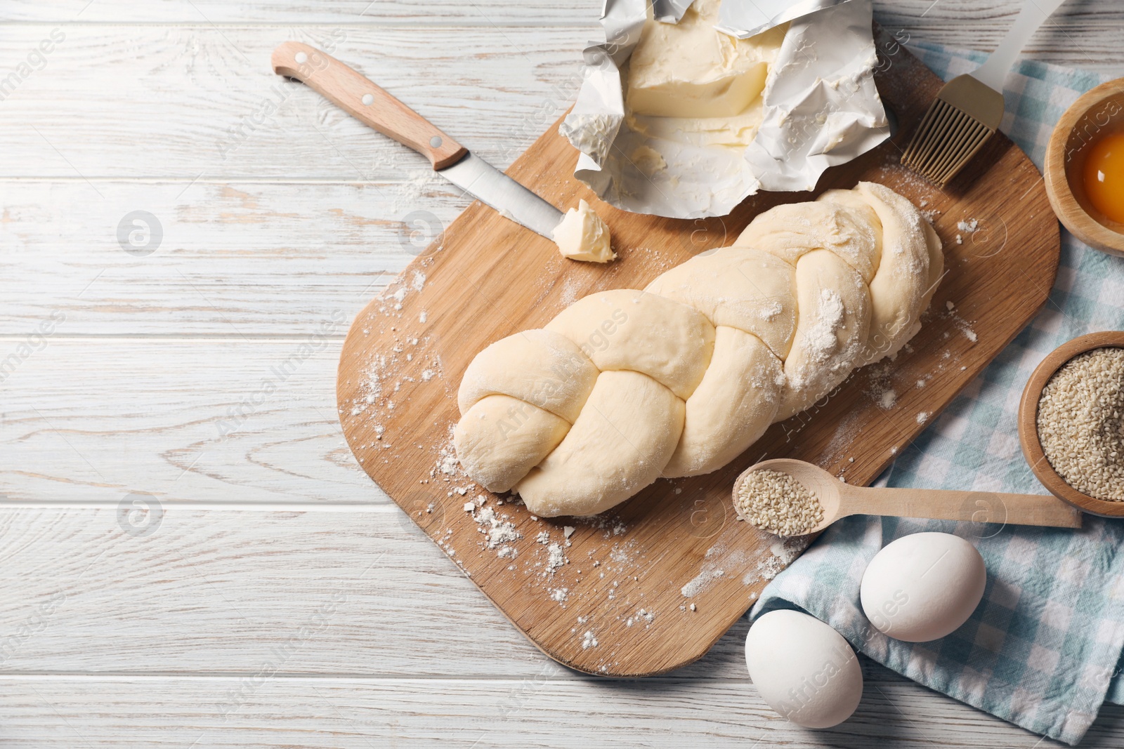 Photo of Raw braided bread and ingredients on white wooden table, flat lay with space for text. Traditional Shabbat challah