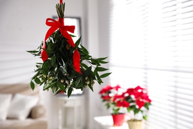 Mistletoe bunch with red bow hanging indoors, space for text. Traditional Christmas decor