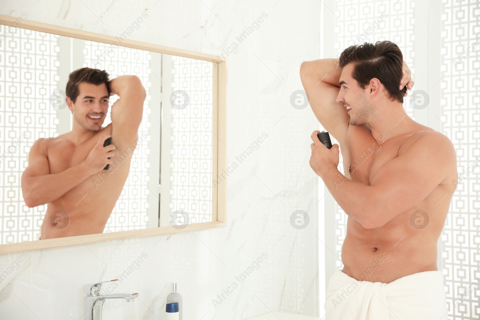 Photo of Handsome young man applying deodorant in bathroom