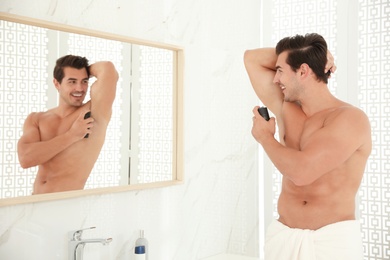 Photo of Handsome young man applying deodorant in bathroom