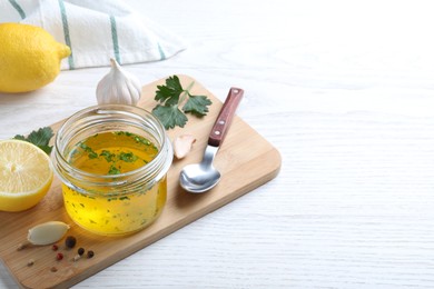 Jar with lemon sauce and ingredients on white wooden table, space for text. Delicious salad dressing