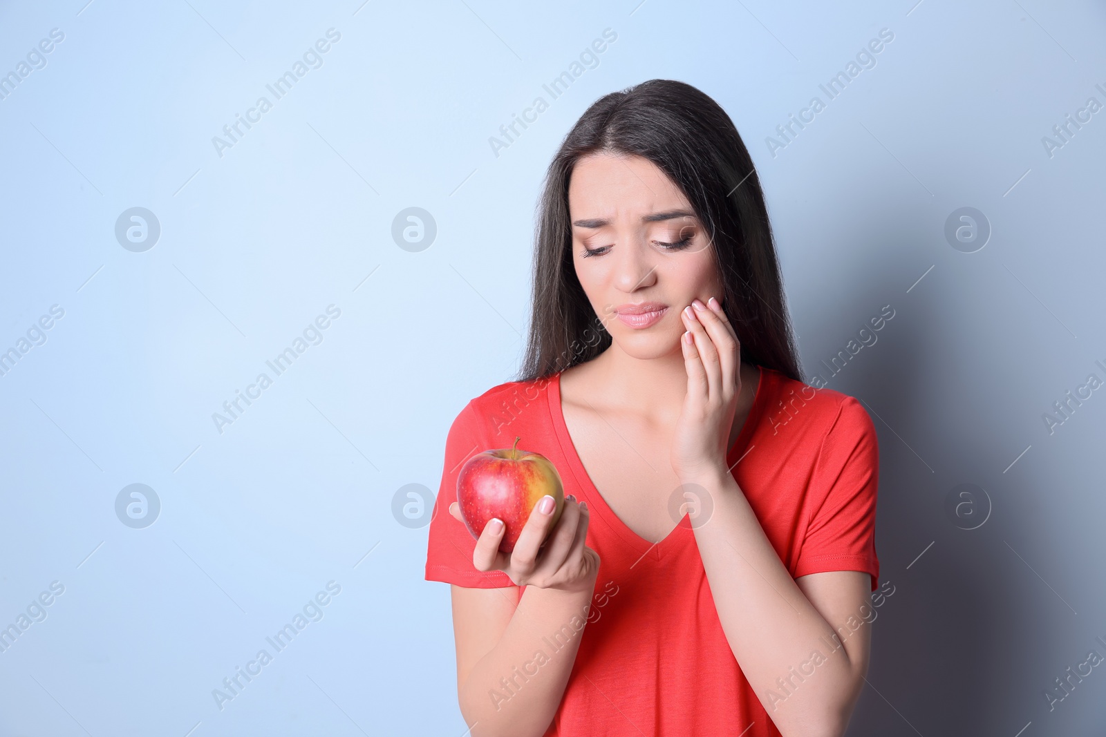 Photo of Woman with sensitive teeth holding apple on color background