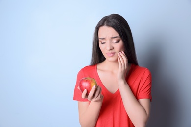 Woman with sensitive teeth holding apple on color background