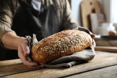 Photo of Man holding loaf of fresh bread at wooden table indoors, closeup