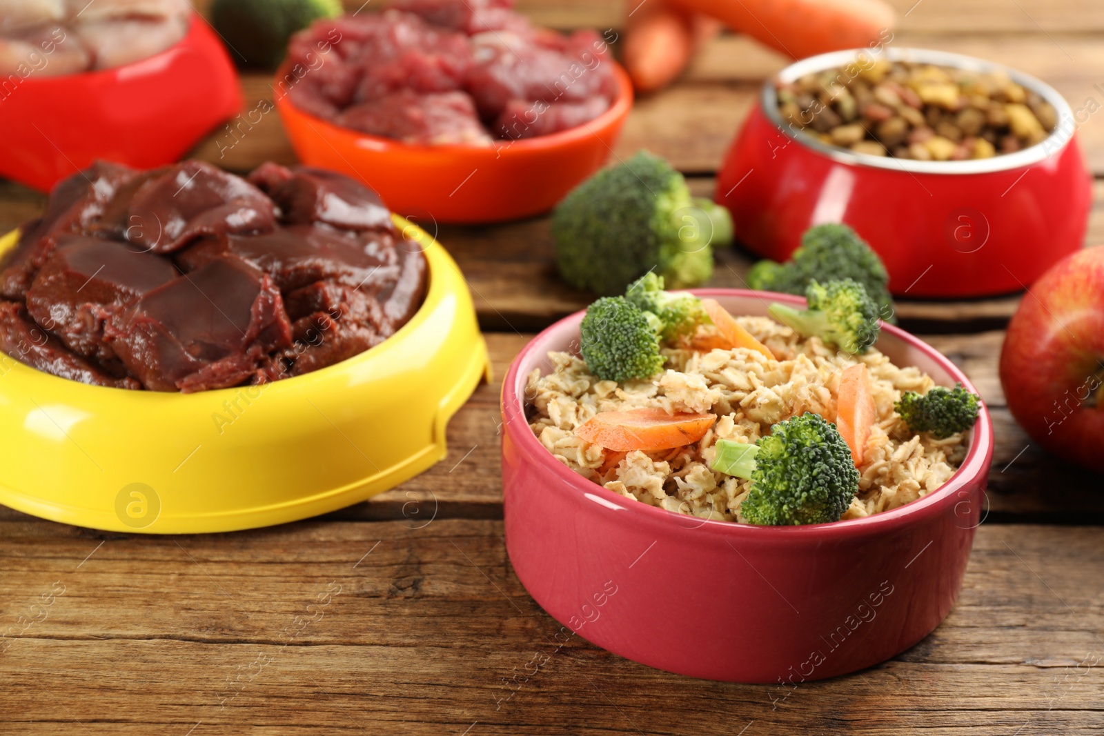 Photo of Natural pet food in feeding bowls on wooden table, closeup