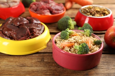 Natural pet food in feeding bowls on wooden table, closeup