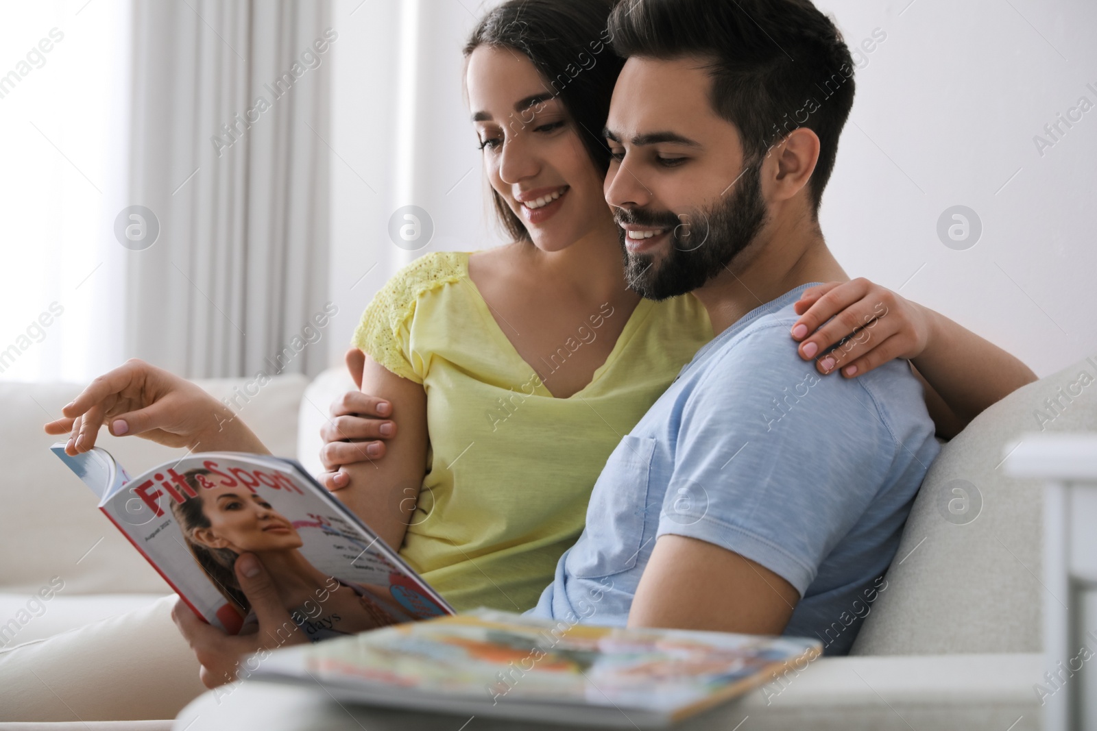 Photo of Young couple reading sports magazine on sofa at home