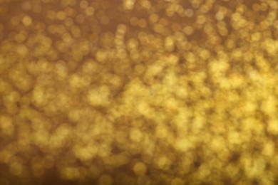 Blurred view of golden glitter on brown background. Bokeh effect