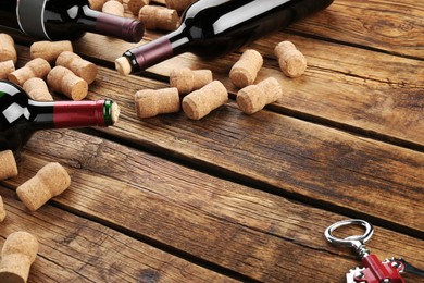 Photo of Bottles with wine, corkscrew and corks on wooden table. Space for text