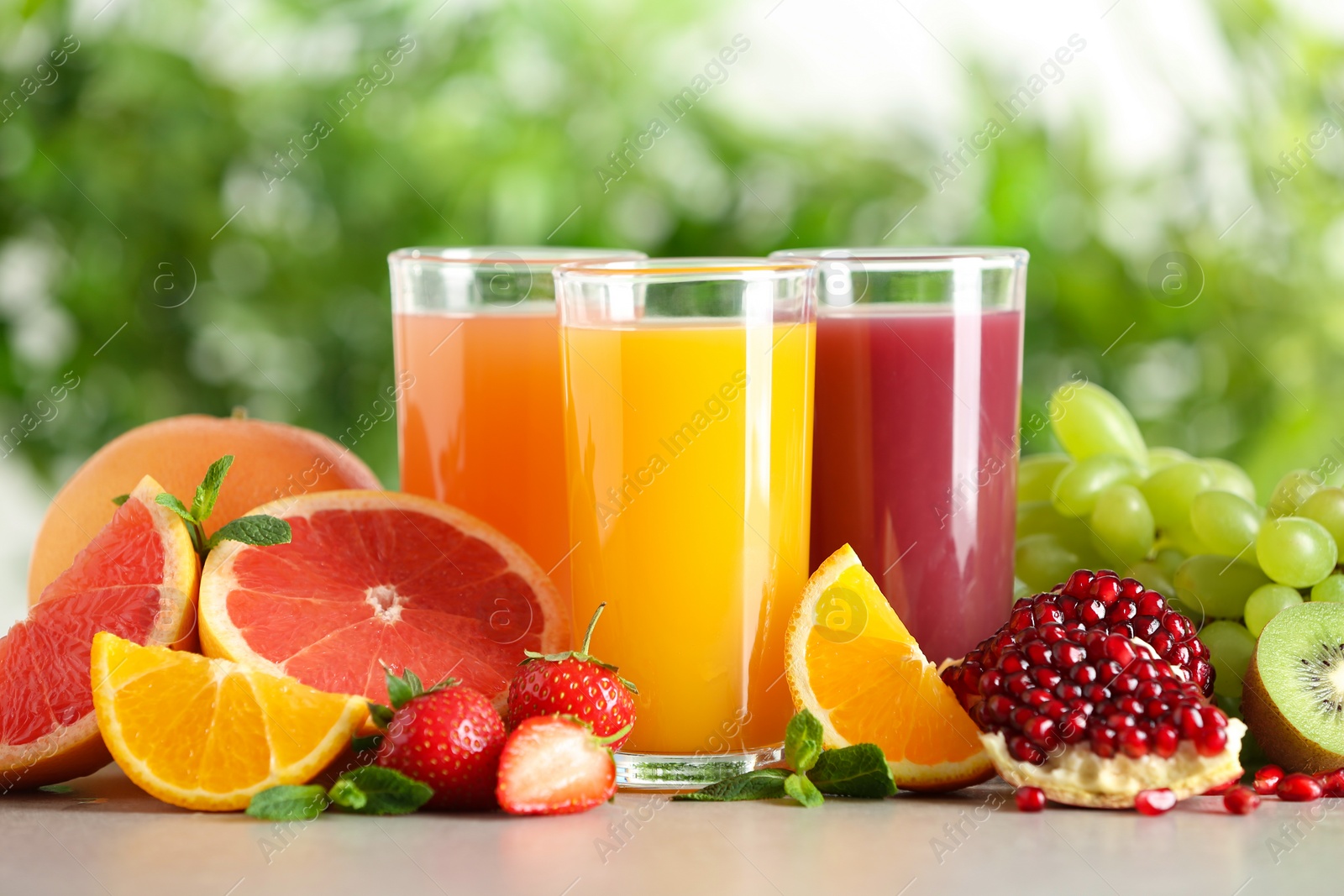 Photo of Three glasses with different juices and fresh fruits on table against blurred background