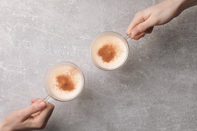 Photo of Women holding glass cups with delicious eggnog at light grey table, top view
