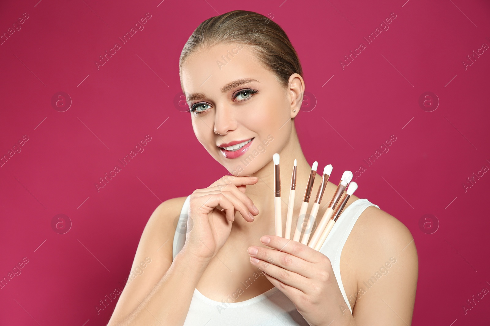 Photo of Beautiful woman with makeup brushes on pink background