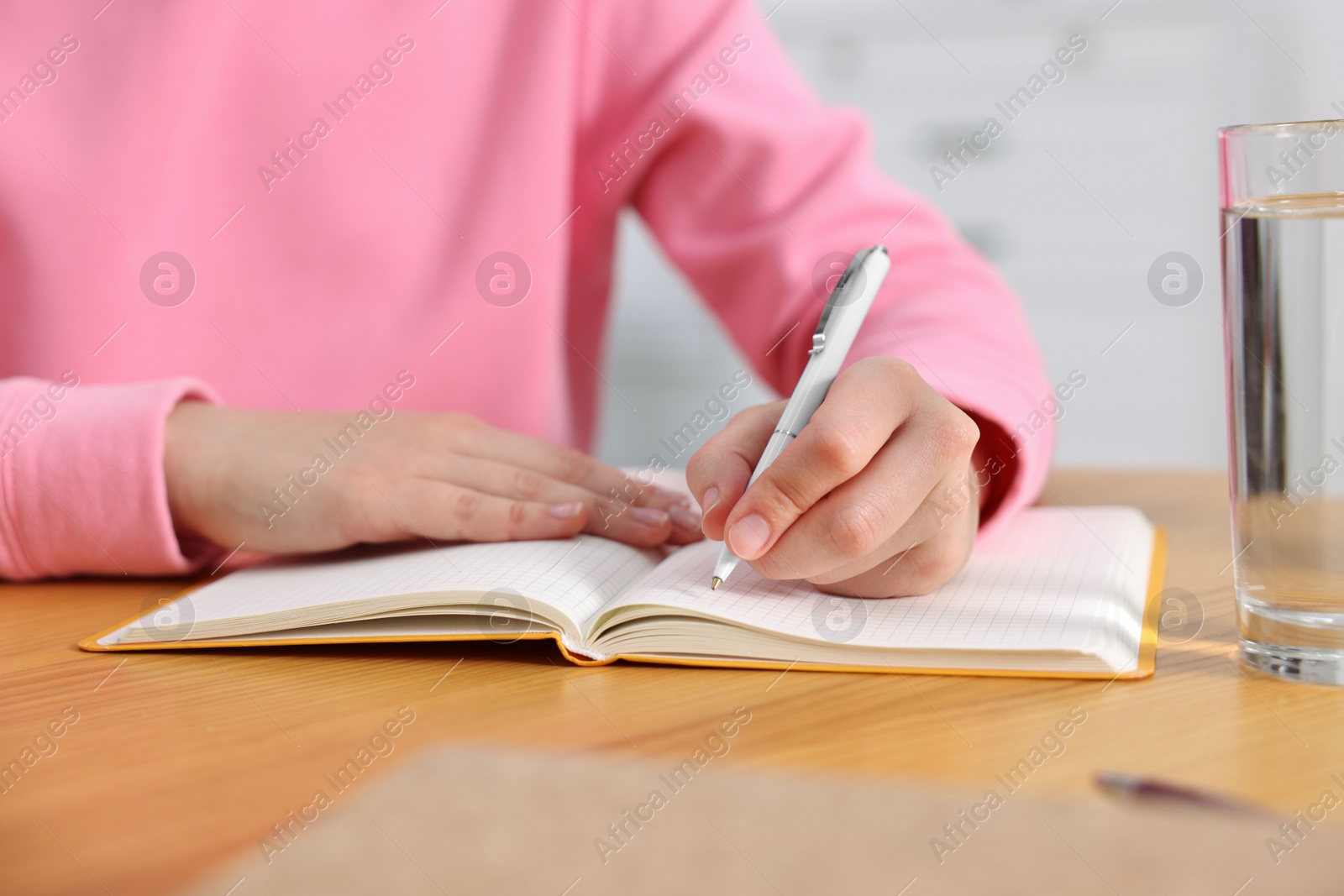 Photo of Young woman writing in notebook at wooden table, closeup