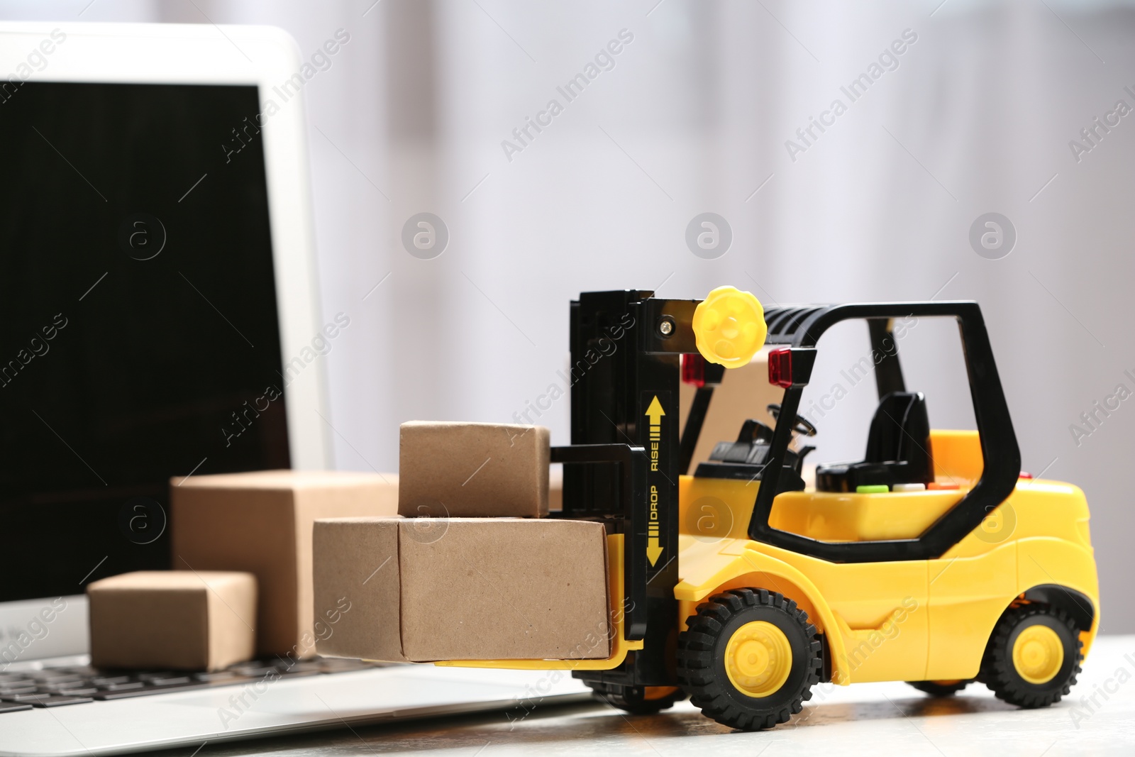 Photo of Toy forklift with boxes near laptop on table. Logistics and wholesale concept