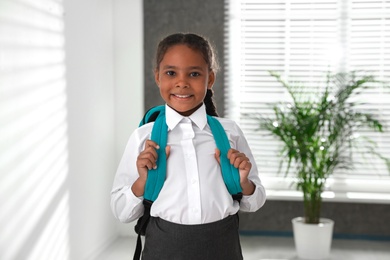 Happy African-American girl in school uniform with backpack indoors