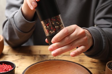 Woman grinding pepper with shaker at wooden table, closeup