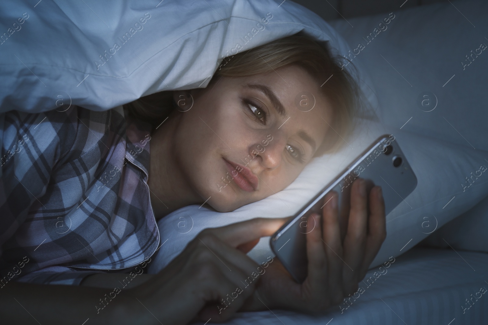 Photo of Young woman using smartphone in bed at night. Nomophobia and sleeping disorder problem