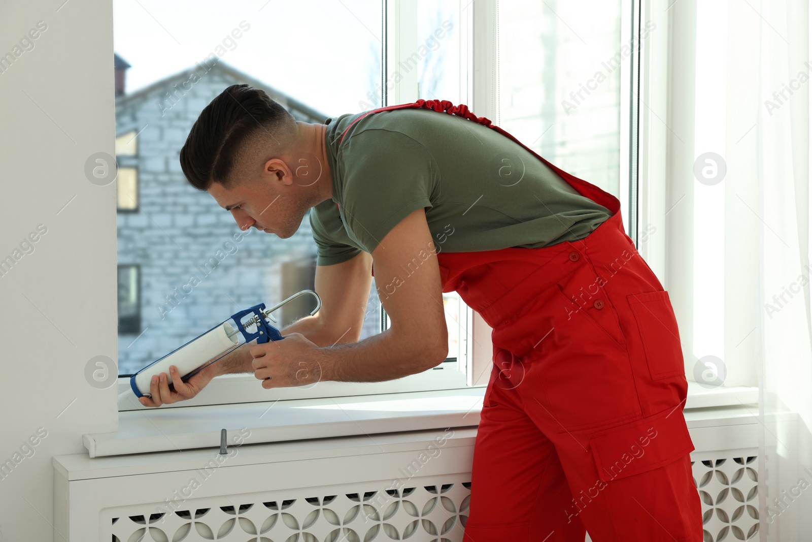 Photo of Construction worker sealing window with caulk indoors