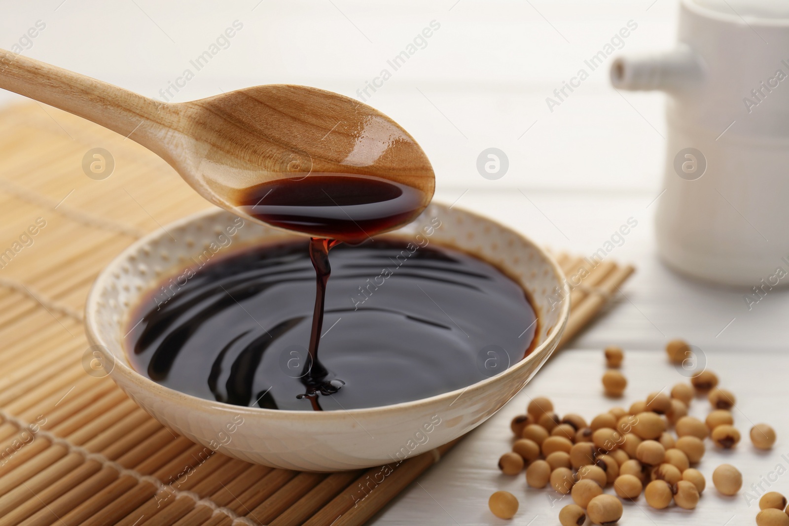 Photo of Taking tasty soy sauce from bowl with spoon on white wooden table, closeup