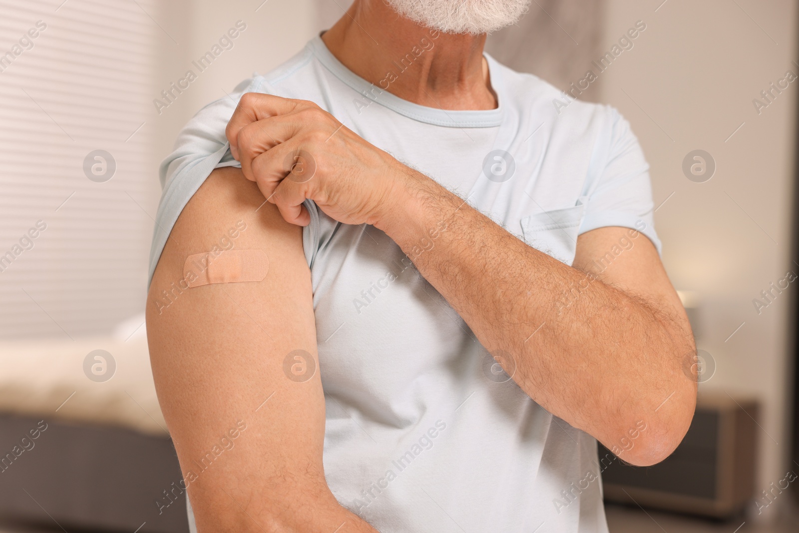 Photo of Man with adhesive bandage on his arm after vaccination indoors, closeup
