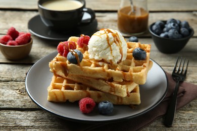 Photo of Delicious Belgian waffles with ice cream, berries and caramel sauce on wooden table, closeup