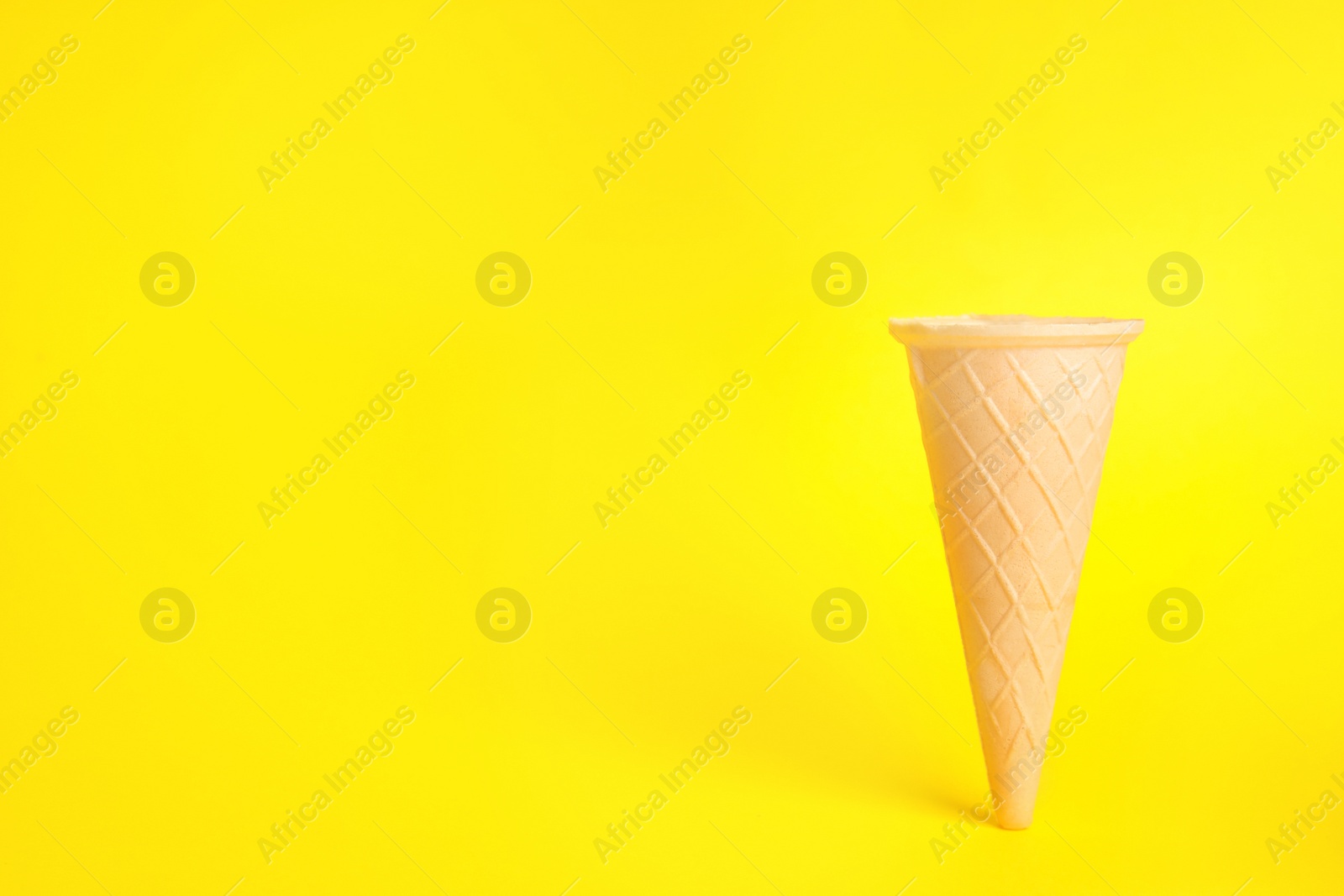 Photo of Empty wafer ice cream cone on yellow background. Space for text