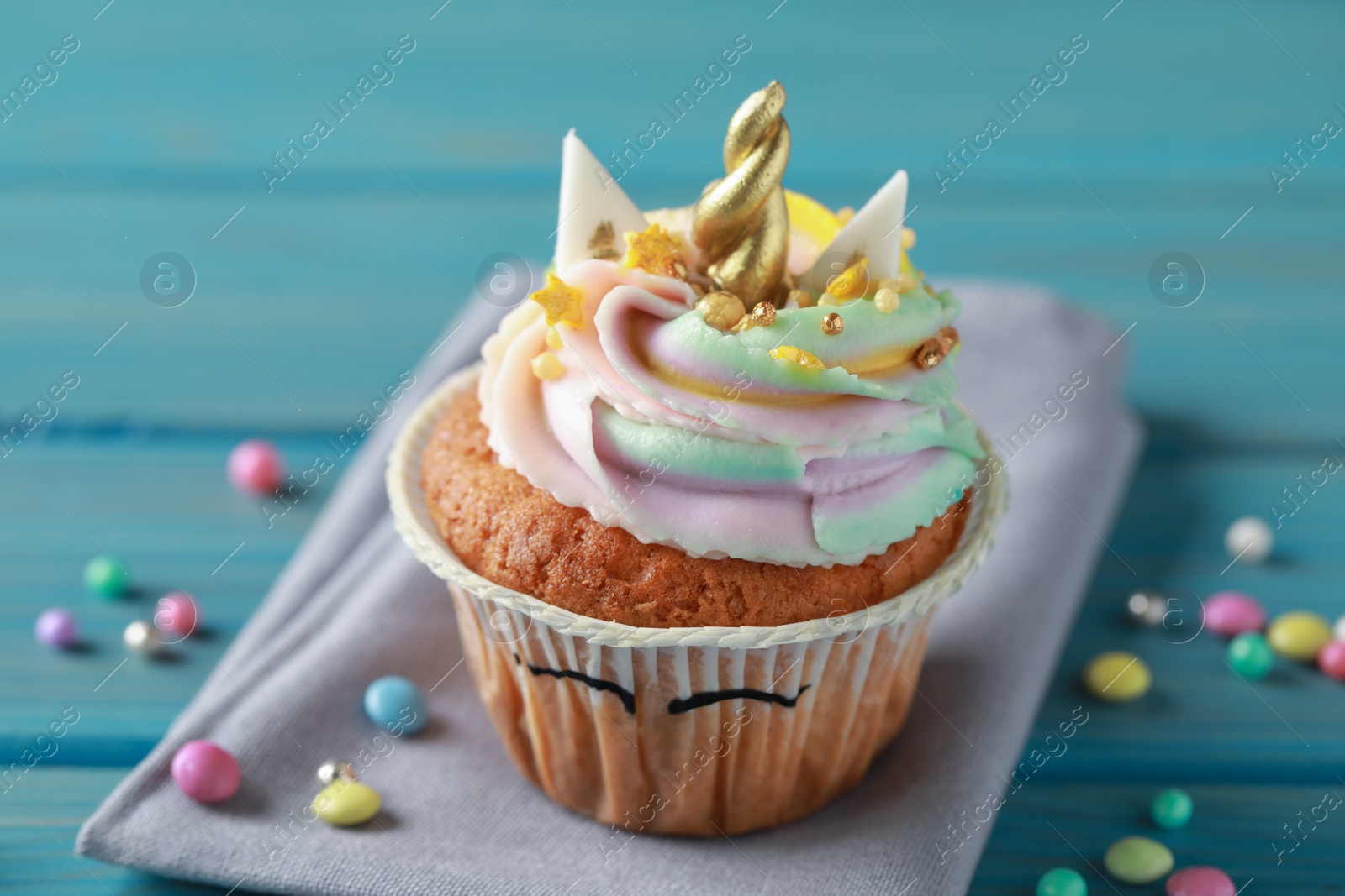 Photo of Cute sweet unicorn cupcake on light blue wooden table, closeup