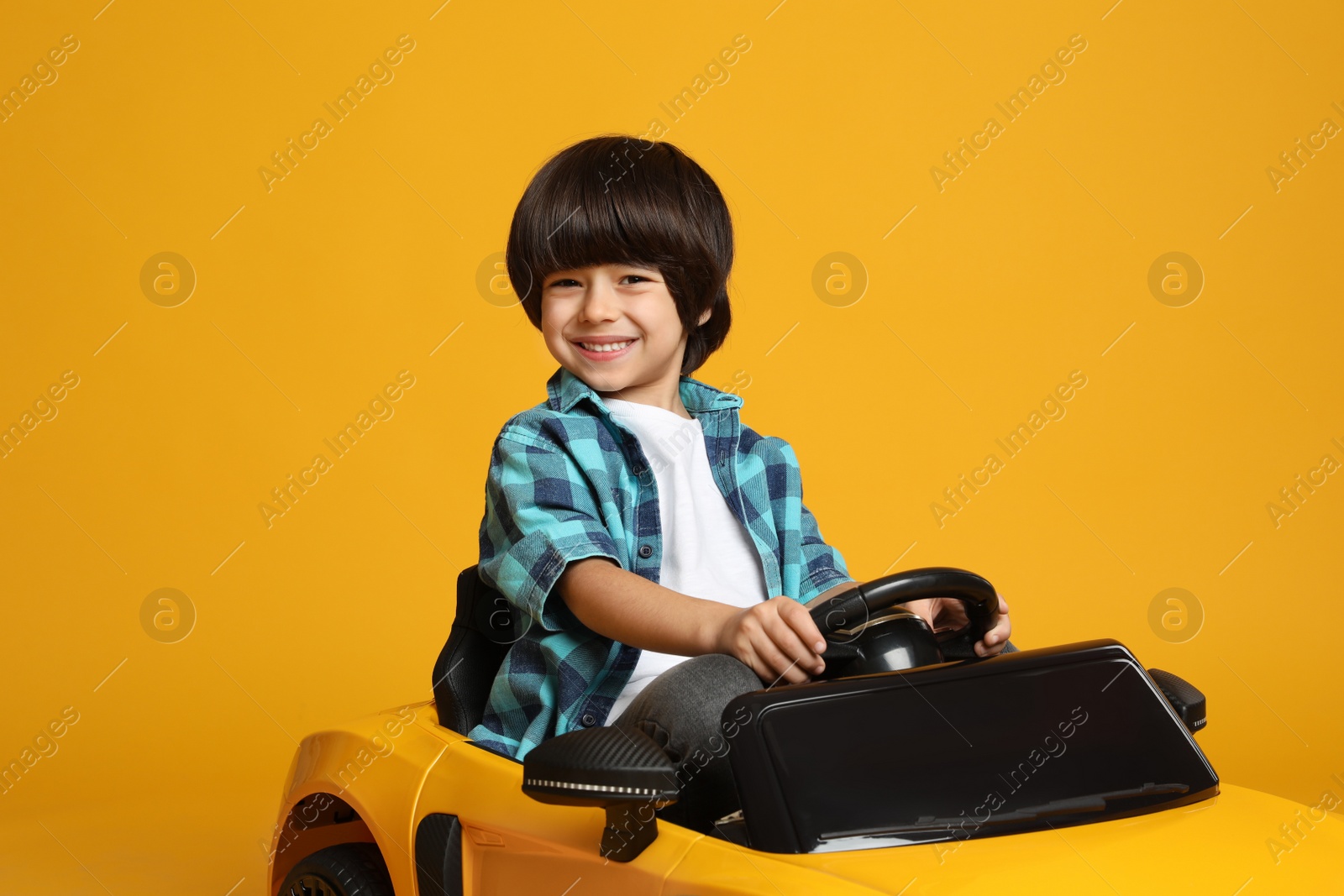 Photo of Cute little boy driving children's electric toy car on yellow background