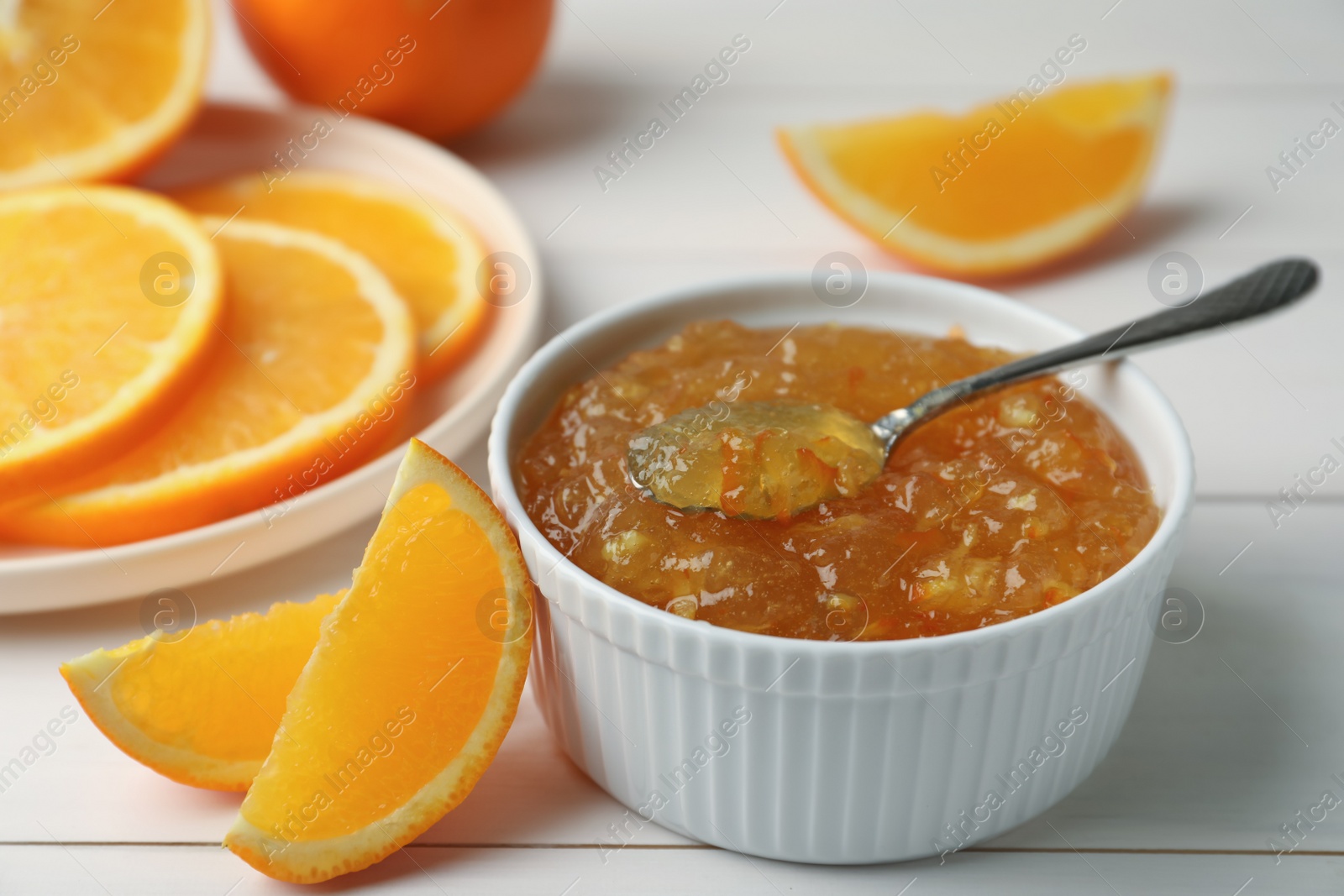 Photo of Delicious orange marmalade in bowl with spoon on white wooden table