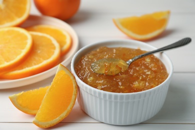 Delicious orange marmalade in bowl with spoon on white wooden table