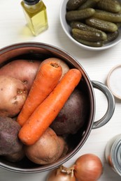 Fresh vegetables and pot on white wooden table, flat lay. Cooking vinaigrette salad