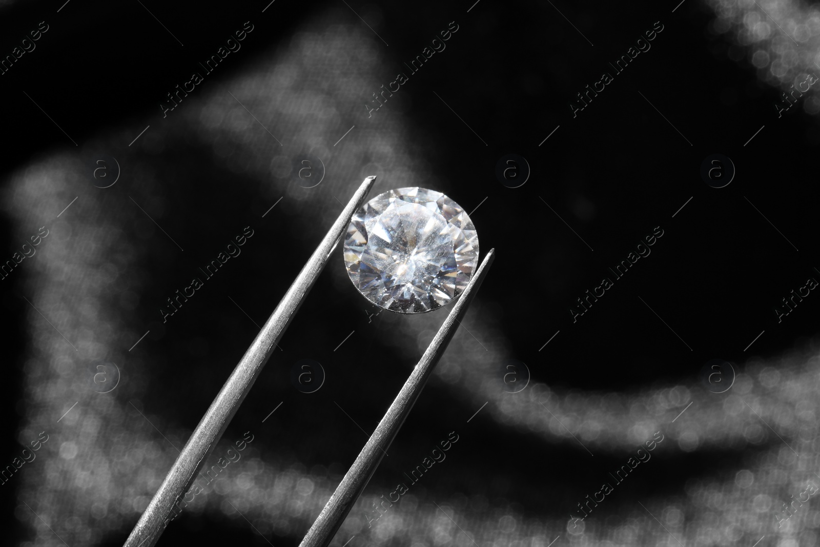 Photo of Tweezers with beautiful shiny diamond on dark background, closeup