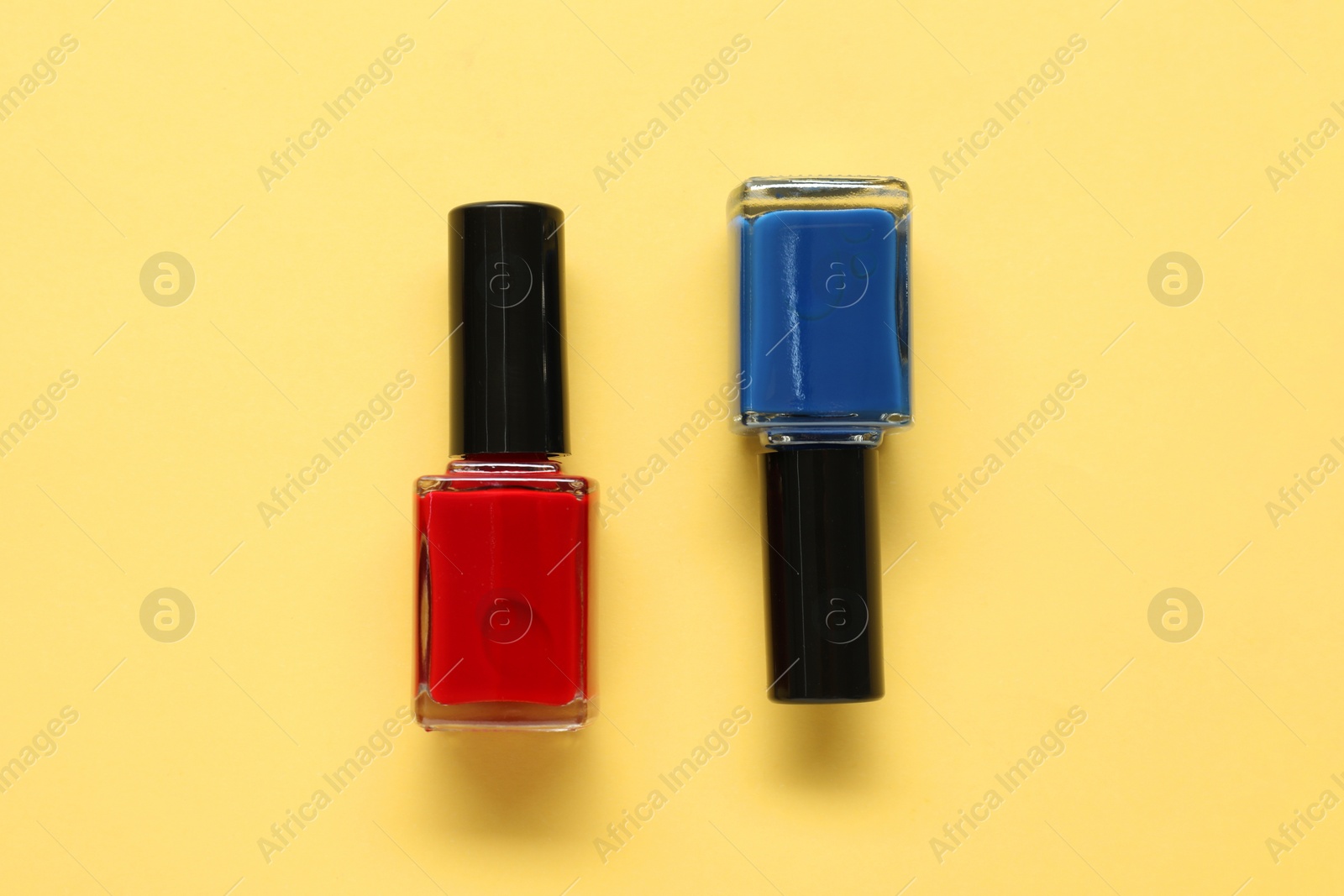 Photo of Bright nail polishes in bottles on yellow background, flat lay