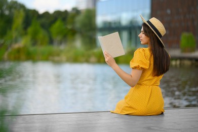 Young woman reading book on pier near lake