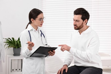 Photo of Doctor with clipboard consulting patient during appointment in clinic