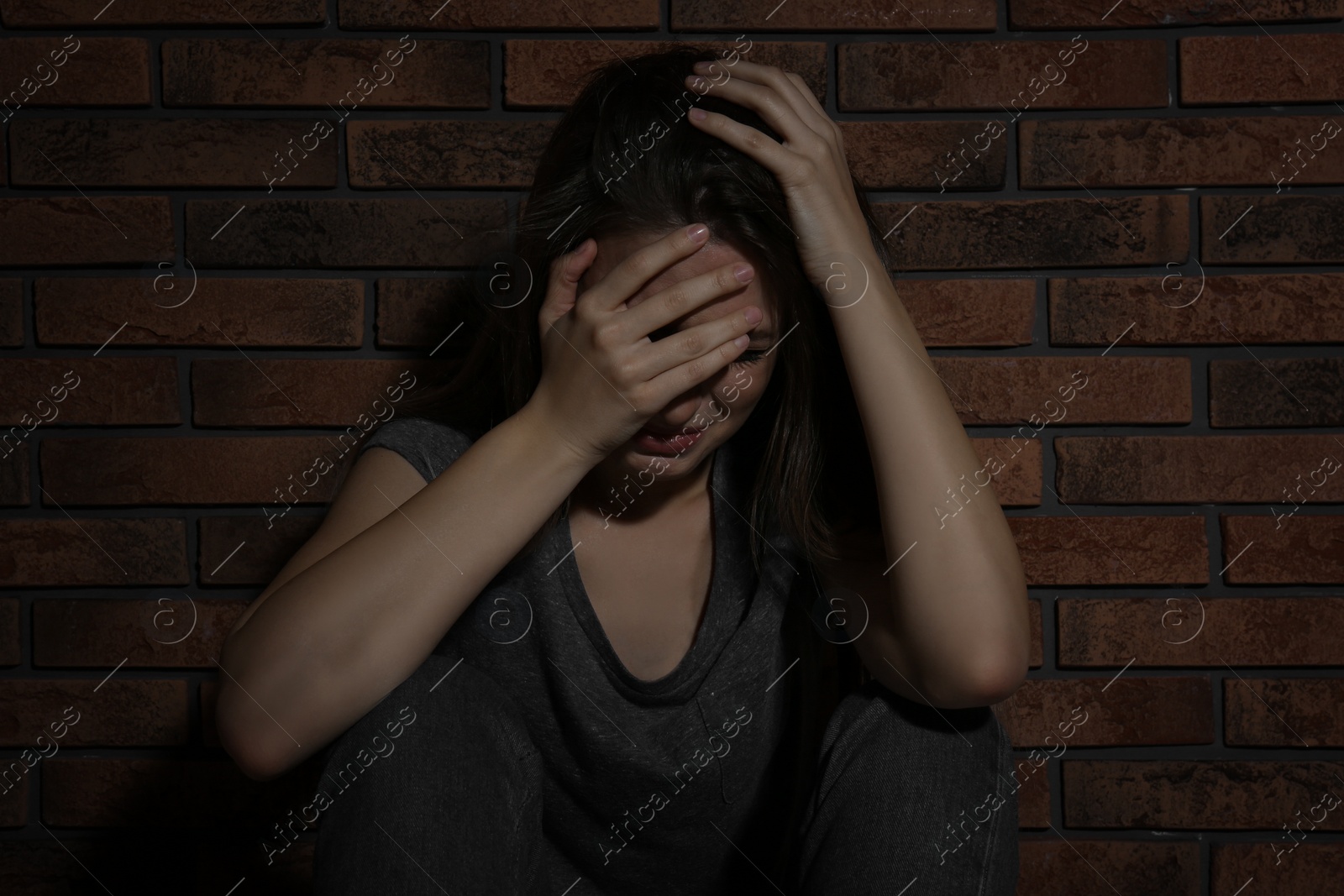 Photo of Abused young woman crying near brick wall. Domestic violence concept