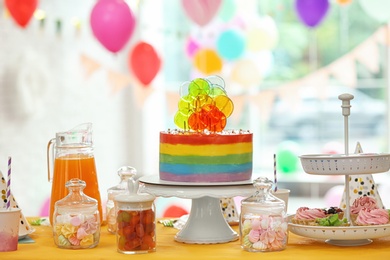 Photo of Bright birthday cake and other treats on table in decorated room