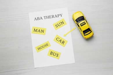 Photo of Taxi car model and paper sheet with phrase ABA Therapy on white wooden table, flat lay