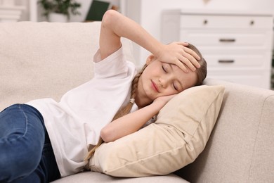 Photo of Little girl suffering from headache on sofa indoors