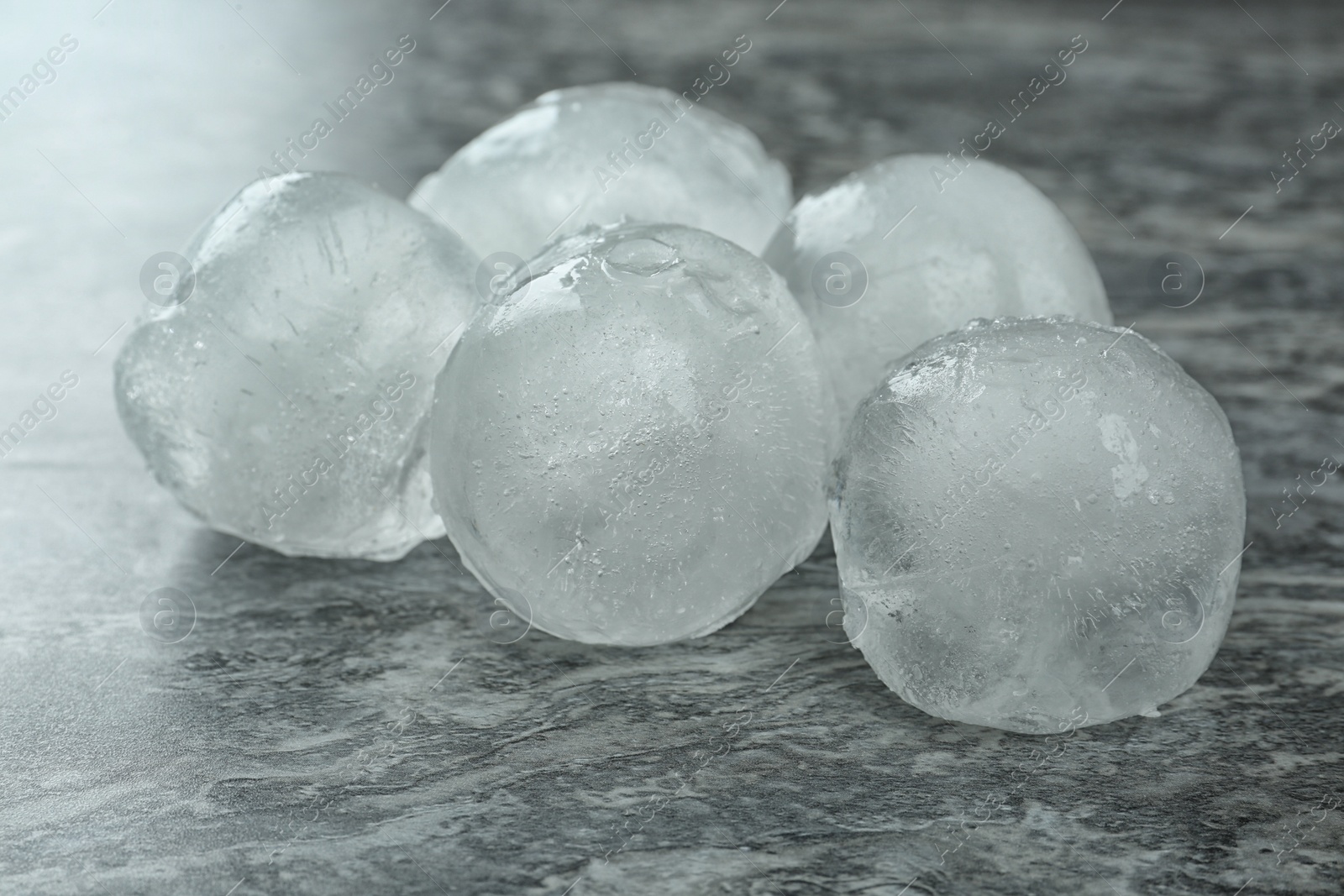 Photo of Many frozen ice balls on grey marble table, closeup